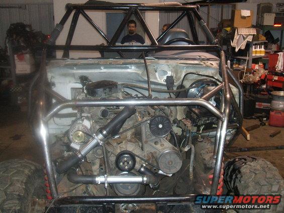 Off-road vehicle with exposed engine and custom roll cage, front view. Muddy tires visible