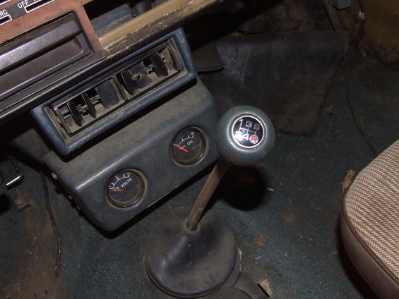 Vehicle interior showing a 4-speed manual transmission shifter, oil pressure gauge, and voltage gauge