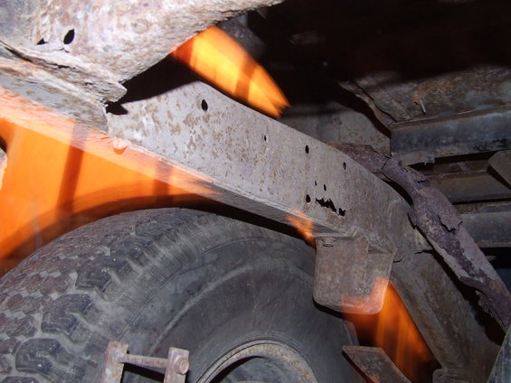 Rusted frame and tire of a vehicle, showing significant corrosion and orange light reflections