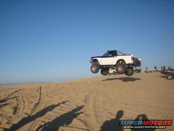 1995 Ford Bronco mid-air jump over a sand dune with other vehicles in the background