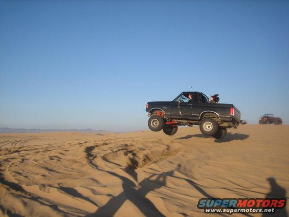 Black 1995 Ford Bronco jumping a sand dune