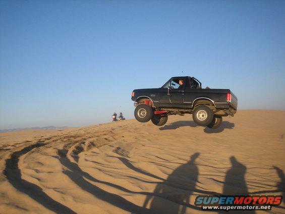 Black 1995 Ford Bronco jumping a sand dune