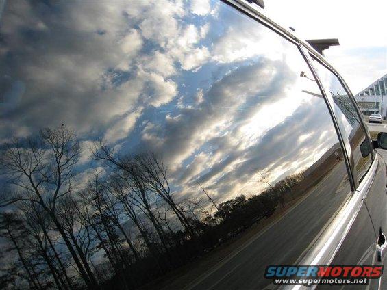 Reflection of sky and trees in the side window of a dark vehicle