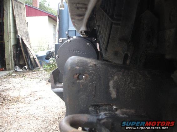 Close-up of a winch mount bolted to a vehicle's front bumper, with a house and garage in the background