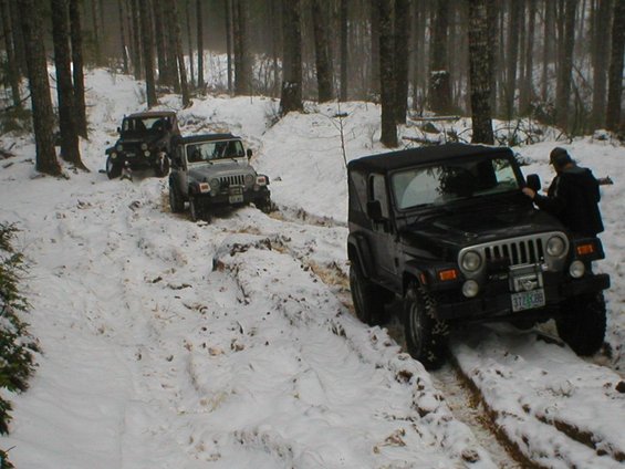 Black 2005 Jeep Wrangler in snow with a person standing next to it, front 3/4 view