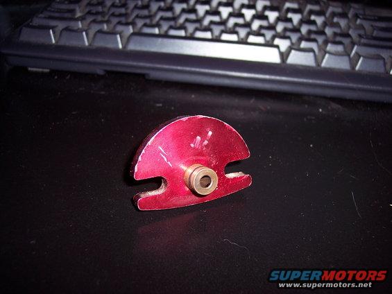 Red metal automotive part with a brass fitting, resting on a black surface with a keyboard in the background