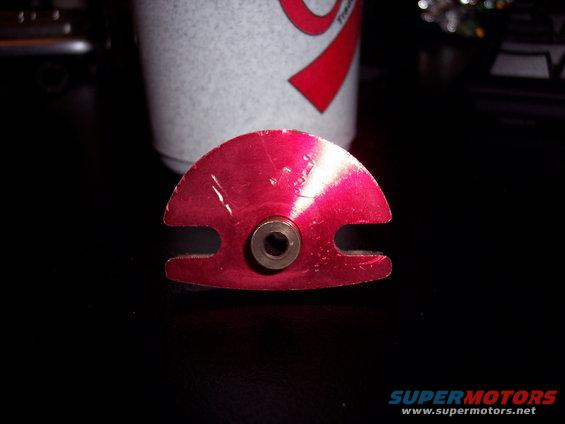 red semicircular metal part with a bolt hole in the center, sitting on a black surface next to a cup