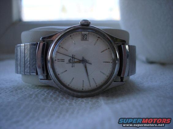 Close-up of a silver wristwatch with a white face and metal band. Date window shows '25'