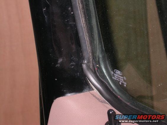 Close-up of a car's door seal and window trim. A Ford logo is visible on the glass