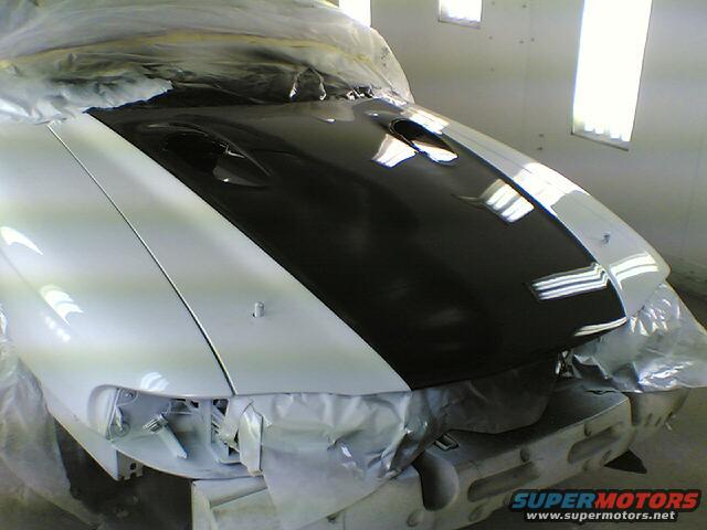 White car with black hood, front view, under repair