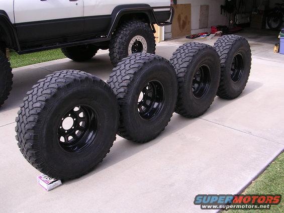 Four off-road tires lined up in front of a lifted SUV with large mud tires