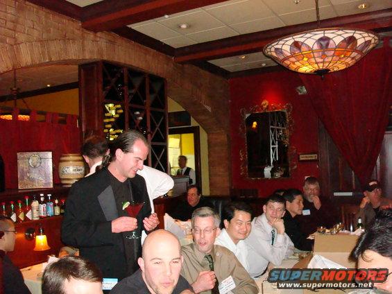 People gathered around tables in a restaurant with red walls and a stained-glass lamp