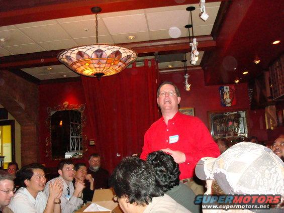 People gathered in a room with a man in a red shirt speaking