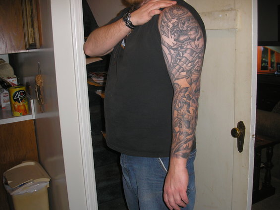 Man with full sleeve tattoo on his right arm, wearing a black t-shirt and blue jeans