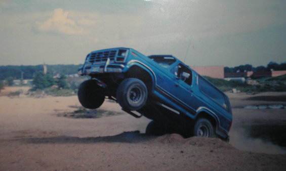 Blue Ford Bronco mid-air, front wheels up, kicking up dirt
