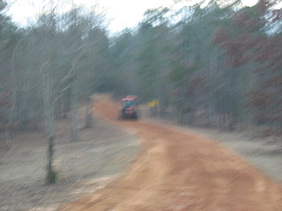 Red tractor driving away on a dirt road through a wooded area
