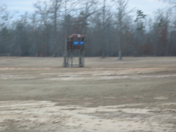 Wooden hunting blind with blue panels stands in a bare field with trees in the background