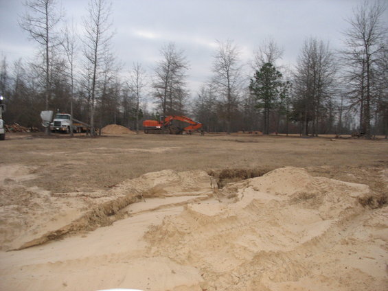 Construction site with orange excavator and white truck near trees