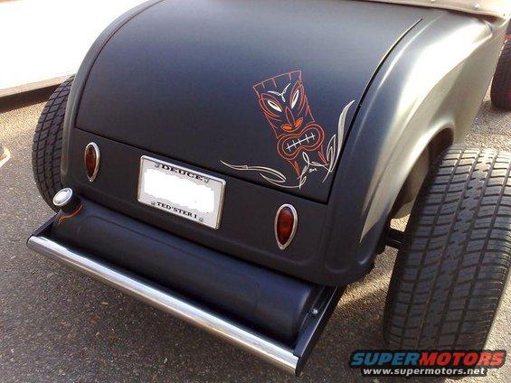 Rear view of a hot rod with a tiki graphic on the trunk and wide rear tires