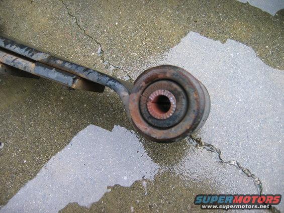 Rusty suspension control arm with a rubber bushing on a wet concrete surface