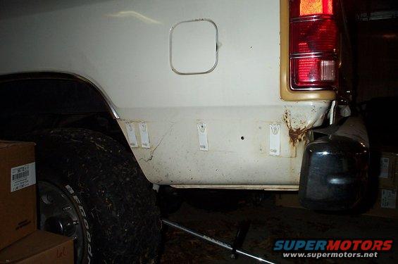 Rear quarter panel and bumper of a white SUV, showing rust and some damage