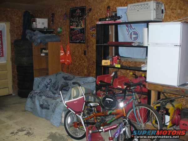 Garage interior with stacked tires, a bed, shelves with a refrigerator, and bicycles