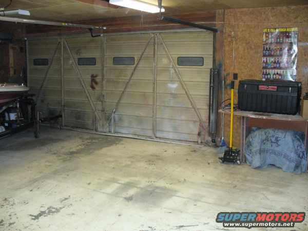Garage with a big closed overhead door, a toolbox on a shelf, and a boat on a trailer to the left
