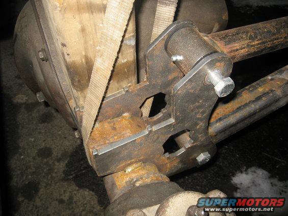 Close-up of a custom-made metal bracket attached to a vehicle's rear axle, secured with a strap