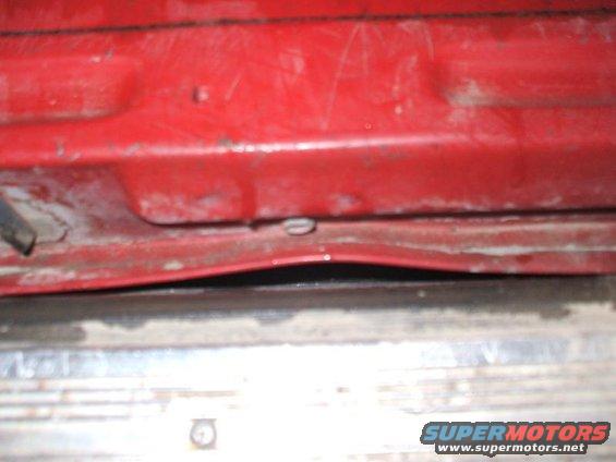 Close-up of a red car door's lower edge, showing a slight dent and a clip. Supermotors.net logo visible