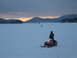1995 Ford Bronco - A snowmobiler rides across a frozen lake at dusk, with other riders and distant mountains visible.