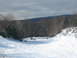 1995 Ford Bronco - Several snowmobiles are parked and in use on a snow-covered hill, with a wooded area and distant hills under a cloudy sky.