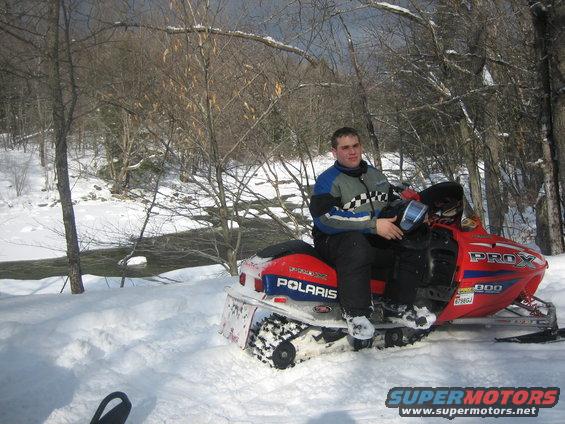 Man sitting on red Polaris snowmobile in snowy woods