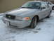 2004 Ford Crown Victoria - A silver Ford Crown Victoria sits in the snow, its front grille and license plate visible.