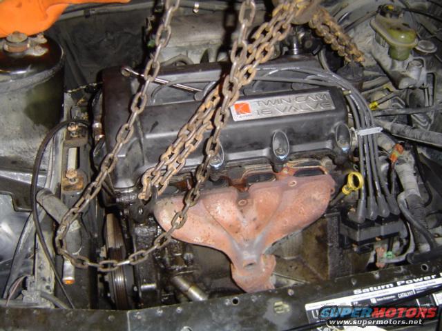 Engine with 'Twin Cam 16 Valve' cover being lowered into engine bay