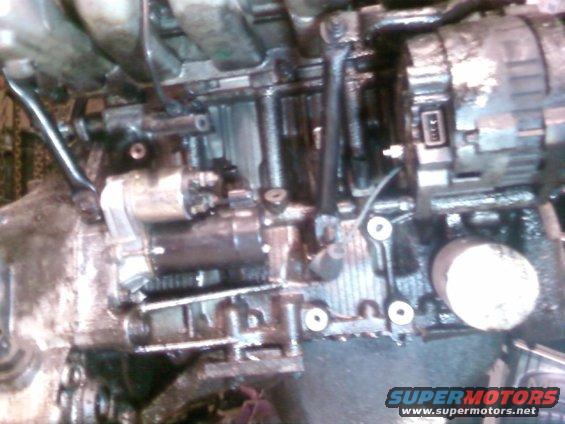 Close-up of engine starter motor and alternator assembly with oil residue