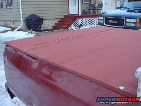 Red wooden truck bed cover over a red truck bed. GMC truck visible in background