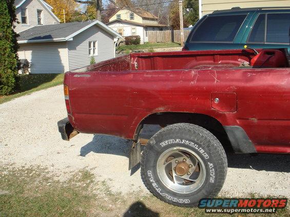 1991 Toyota Tacoma rear quarter panel, tire, and bed. Green SUV parked behind
