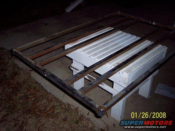 Metal rack frame with wooden slats on white sawhorses, outdoors at night