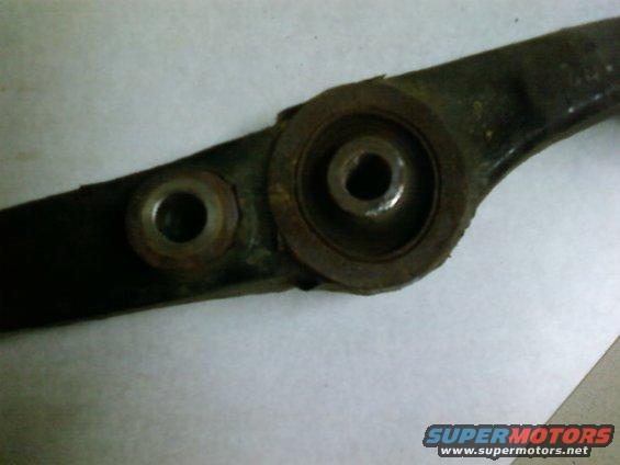 Close-up of a rusty suspension control arm showing two mounting points with bushings