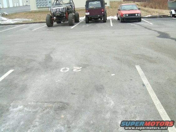 Off-road buggy, maroon Jeep Wrangler, and red Volkswagen Golf parked in a lot