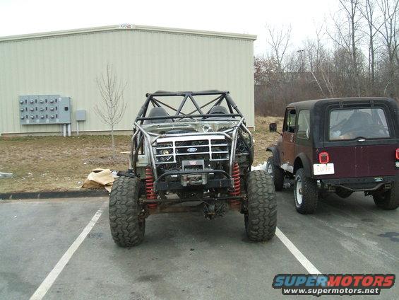 Custom buggy with roll cage and big tires parked next to a Jeep