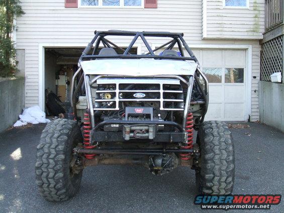 Custom buggy with roll cage, large tires, and winch in front of a garage. Grille appears to be from a 1995 Ford Bronco