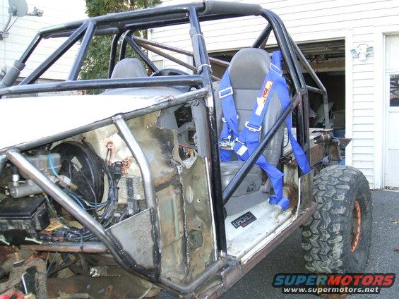 Custom buggy interior with roll cage, racing harness, and exposed engine bay. 'BRONCO' badge visible on door sill