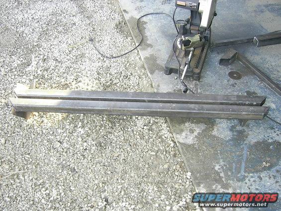 Two metal sliders resting on gravel next to a chop saw