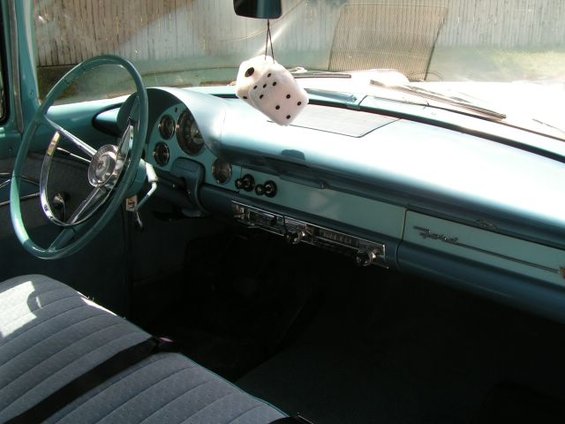 1956 Ford Fairlane interior showing dashboard, steering wheel, and fuzzy dice hanging from rearview mirror