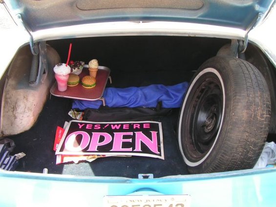Trunk of a car with a tray of fast food, a spare tire, and an 'Open' sign