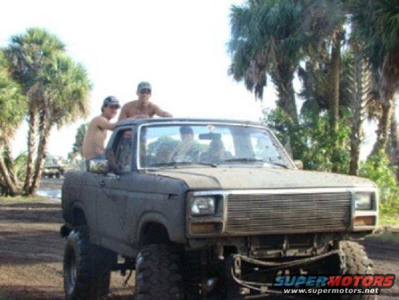 Gray Ford Bronco with lifted suspension and large tires, front grille is visible, with three people in and on the vehicle