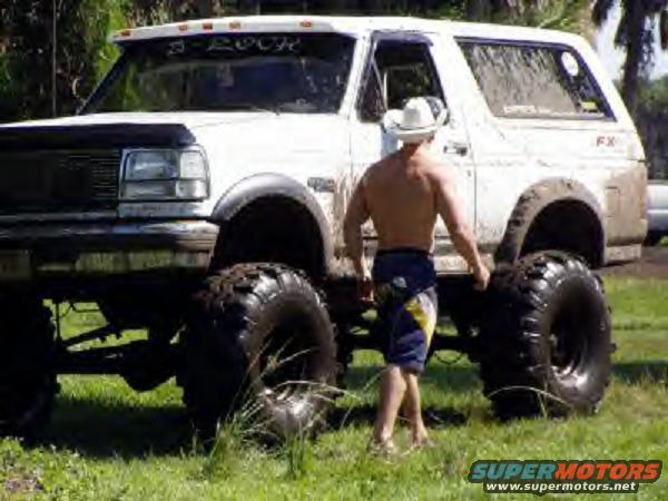 White 1995 Ford Bronco with oversized tires and a man in a cowboy hat standing next to it