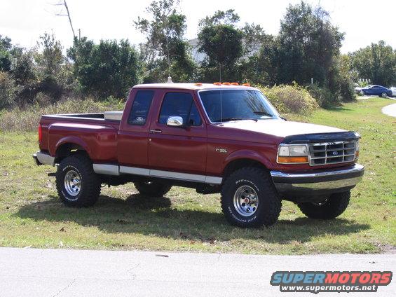Red Ford F-150 pickup truck, lifted with off-road tires. Hood has a bug deflector
