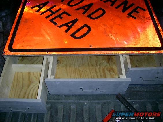 Storage drawers installed in the bed of a pickup truck, beneath an orange road sign